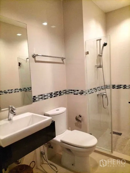 Condominium for rent in Ratchathewi, Bangkok - Bright bathroom with glass shower enclosure, vanity basin and toilet.