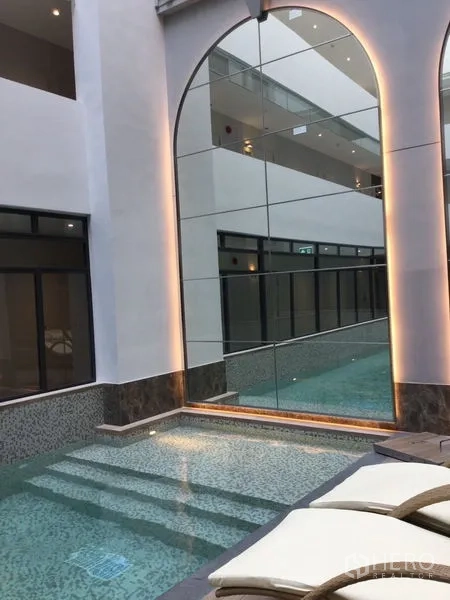 Condominium for rent in Watthana, Bangkok - Resort-style pool zone with arched mirrored wall, shallow steps and sun loungers.