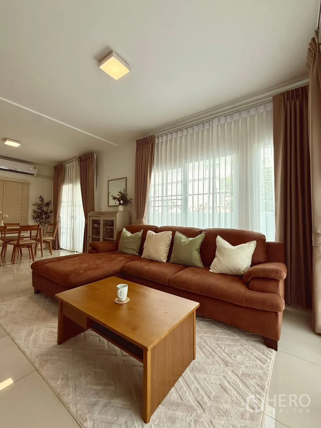 Detached House for rent in Bang Phli, Samut Prakan - Living area with brown sectional, coffee table, and floor-to-ceiling draped windows.