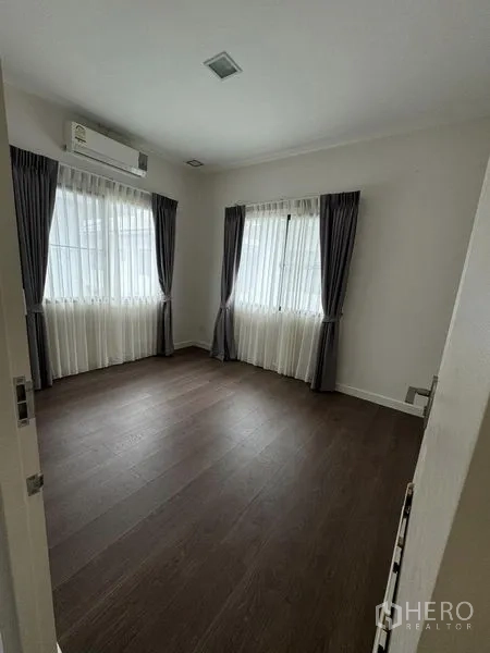 Detached House for rent in Samut Prakan - Corner bedroom with two windows, air conditioner and double curtains.