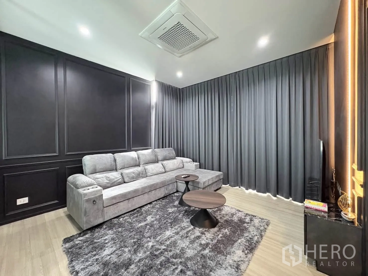 独栋房屋 for rent in Saphan Sung, Bangkok - 家庭影音休闲室，长条灰色沙发、地毯与深色装饰墙。