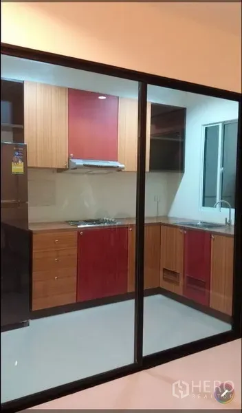 Townhouse for rent in Suan Luang, Bangkok - Enclosed kitchen behind glass partition with upper and lower cabinets, cooktop with hood, and sink.
