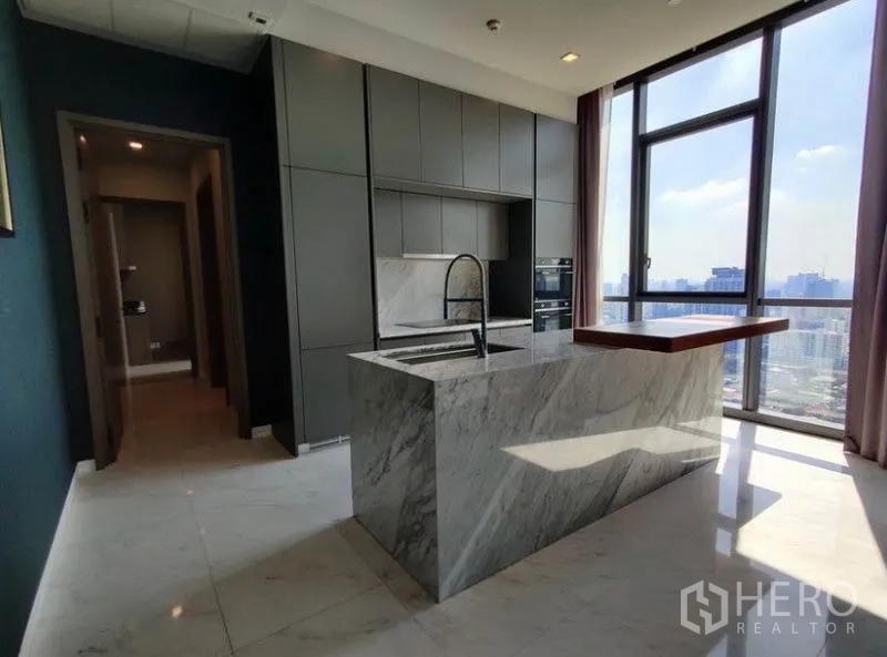 Condominium for rent in Watthana, Bangkok - Modern kitchen with marble island, built-in cabinetry, and a tall window bringing in natural light.