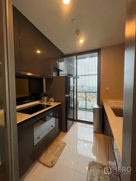 Condominium for rent in Khlong Toei, Bangkok - Modern enclosed kitchen with glossy cabinets, built-in hob, full-size fridge and balcony access.
