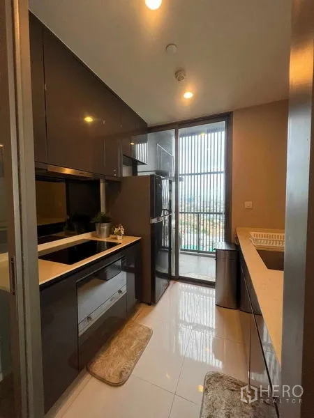 Condominium for rent in Khlong Toei, Bangkok - Modern enclosed kitchen with glossy cabinets, built-in hob, full-size fridge and balcony access.