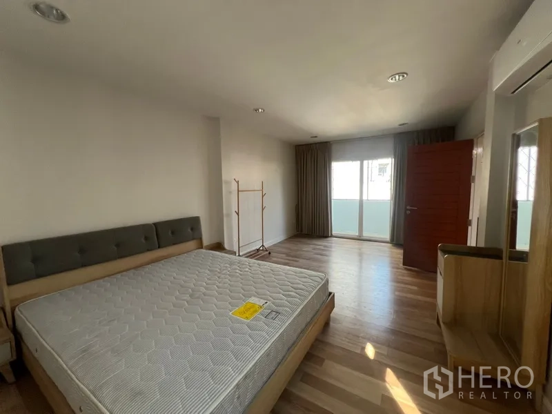Townhouse for rent in Din Daeng, Bangkok - Large bedroom with balcony doors, curtains and bed set on wood-look flooring.