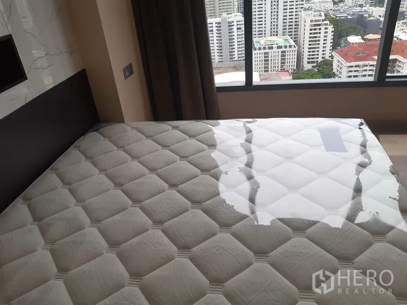Condominium for rent or sale in Watthana, Bangkok - Bedroom with large mattress and panoramic city view through wide window.