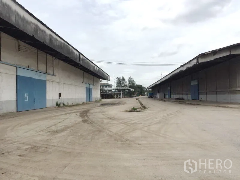 货栈 出租在Pathum Thani - 两座大型混凝土仓库之间的宽阔卡车回转场，配蓝色滑门。