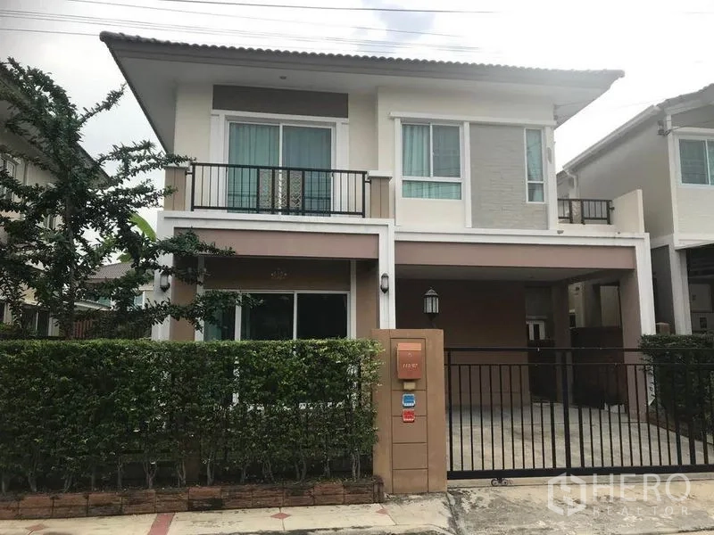Detached House for rent in Bang Phli, Samut Prakan - Two-storey detached house exterior with gated carport, balcony and trimmed hedges.
