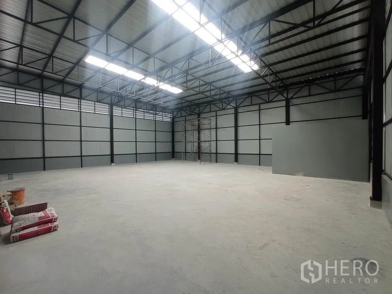 Warehouse for rent in Saphan Sung, Bangkok - Spacious warehouse interior featuring a high steel truss roof with skylights and a smooth concrete floor.