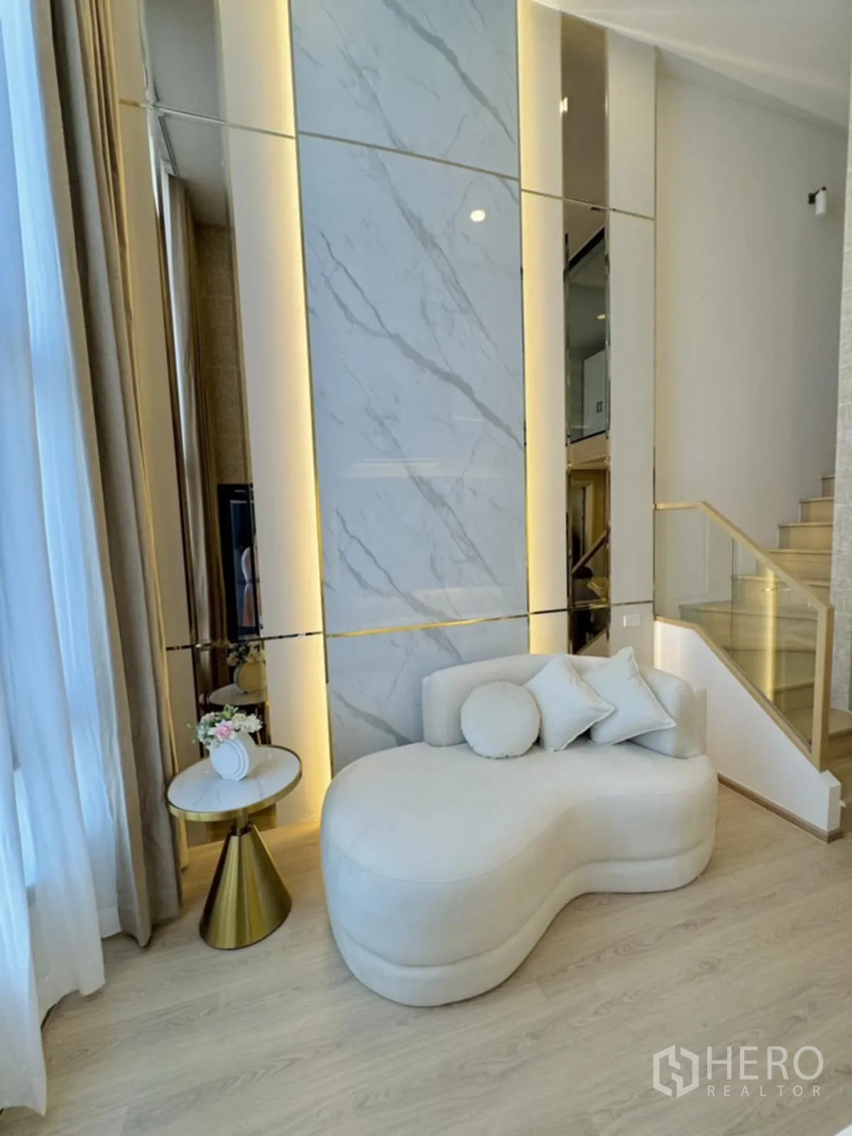 คอนโด for rent in Khlong Toei, Bangkok - พื้นที่นั่งเล่นสว่างด้วยโซฟาเชสสีครีม ผนังลายหินอ่อนพร้อมไฟซ่อน พื้นไม้โทนอ่อน และบันไดราวกระจก