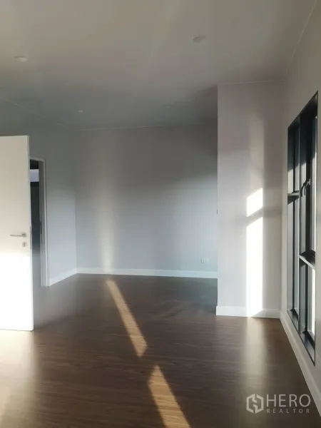 Detached House for sale in Lam Luk Ka, Pathum Thani - Bright empty living space with wood-look flooring, white walls and large black-framed windows.