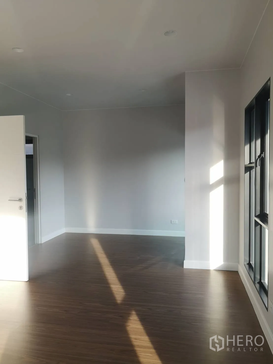 Detached House for sale in Lam Luk Ka, Pathum Thani - Bright empty living space with wood-look flooring, white walls and large black-framed windows.