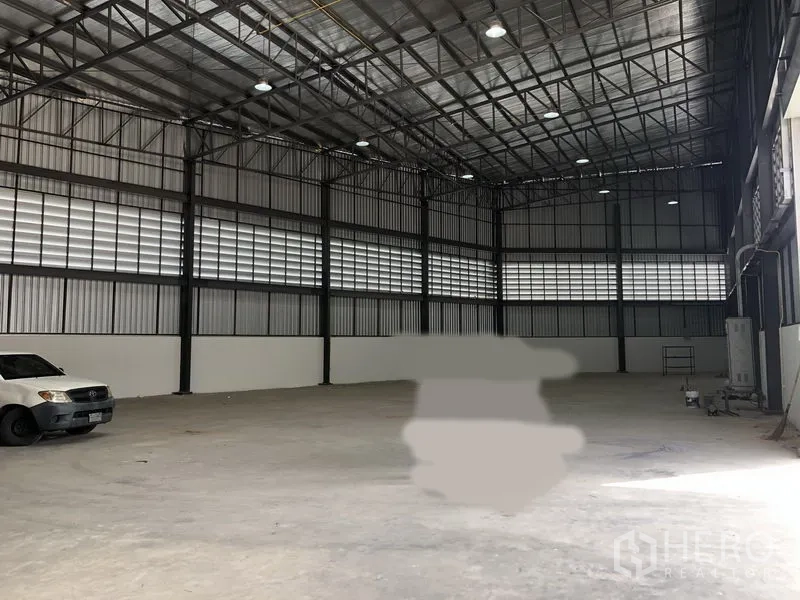 Factory for rent in Samut Prakan - High-ceiling warehouse interior with steel trusses and polished concrete floor.