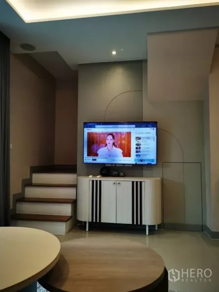Townhouse for rent in Bang Phli, Samut Prakan - Contemporary living area with wall-mounted TV, built-in cabinet and staircase with recessed lighting.