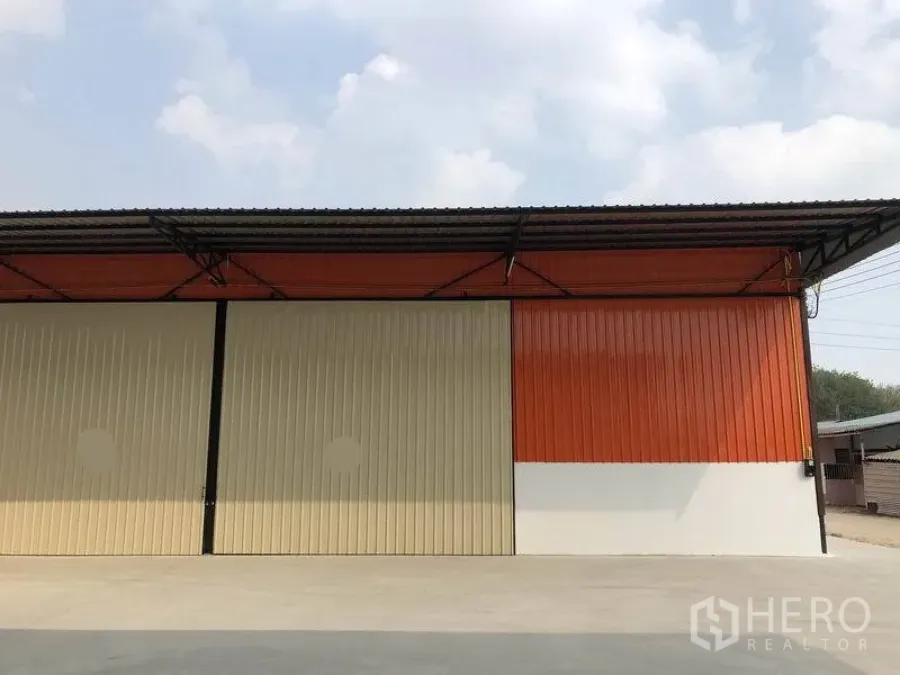 Warehouse for rent in Pathum Thani - Exterior facade of the warehouse with orange cladding, closed sliding doors and a concrete forecourt.