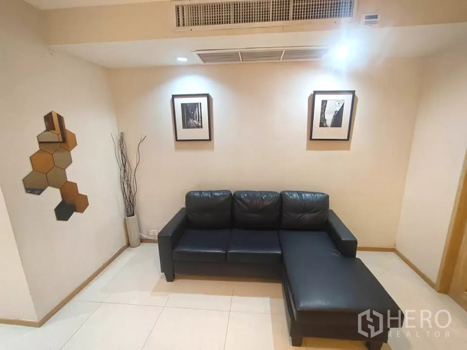 Condominium for rent in Khlong Toei, Bangkok - Cozy living room featuring a black leather sectional sofa, wall art, and recessed lighting.