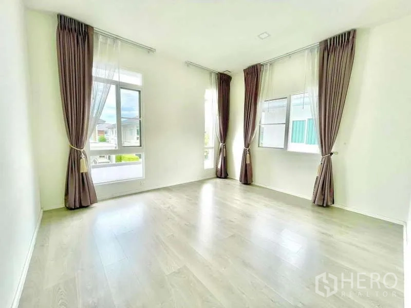 Detached House for rent in Prawet, Bangkok - Bright corner bedroom with large windows, sheer curtains and light wood floors.