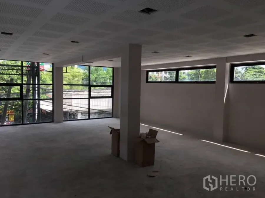 零售空间 出租在Huai Khwang, Bangkok - 开放式零售楼层，转角大玻璃窗，可见街景与绿树。