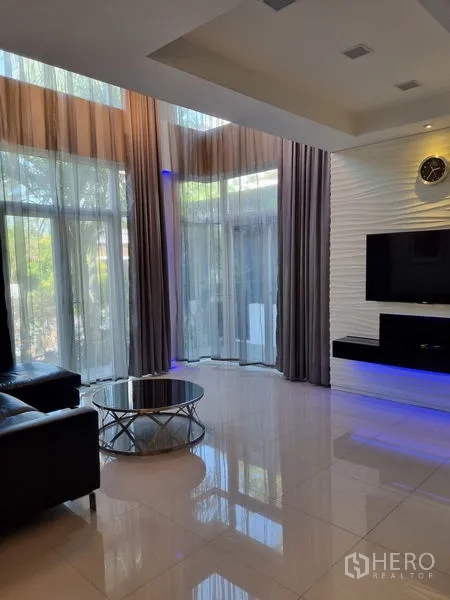 Detached House for sale in Chatuchak, Bangkok - Living room with floor-to-ceiling curtains, glossy tiles and a TV feature wall.