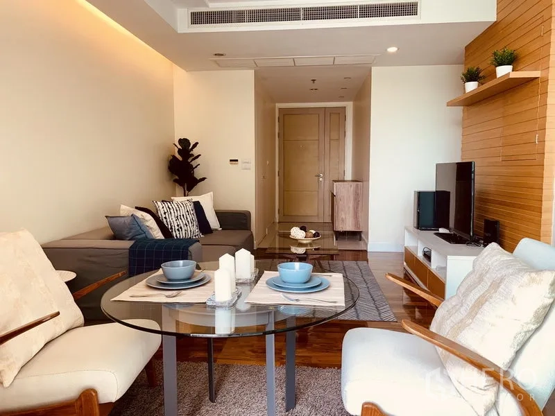 公寓 出租在Watthana, Bangkok - 明亮客厅，玻璃餐桌、木地板与电视墙的公寓内部
