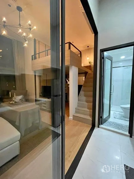 Condominium for rent in Ratchathewi, Bangkok - Entry view to loft-style living room with staircase and a glass-walled bathroom nearby.