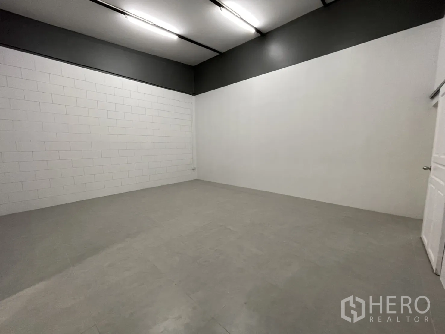 Warehouse for rent in Lam Luk Ka, Pathum Thani - Clean ancillary room with white block walls, grey accent band and tiled floor under strip lighting.