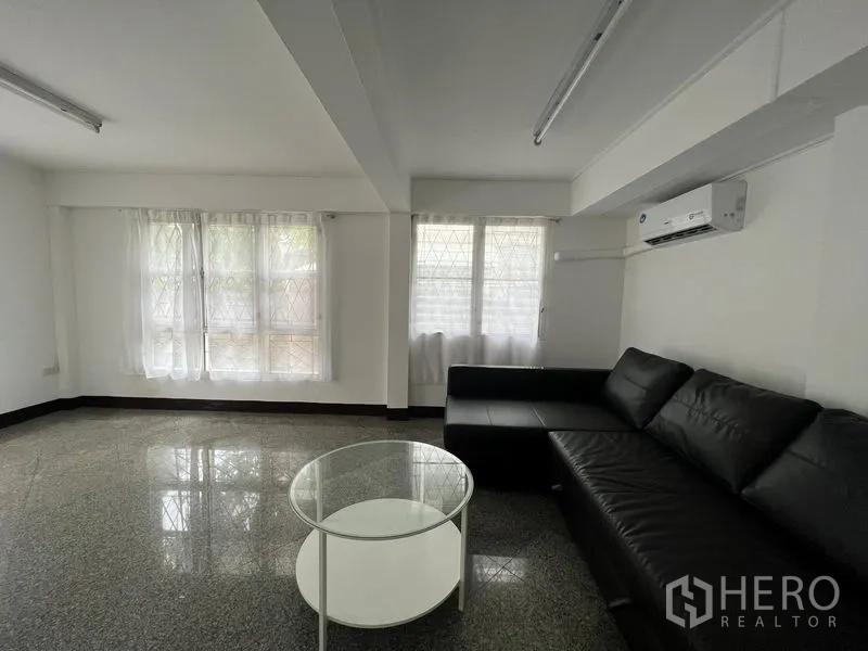 Detached House for rent in Saphan Sung, Bangkok - Living area with black sectional sofa, glass coffee table and multiple windows.