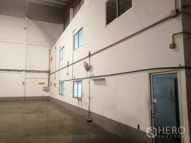 Factory for rent or sale in Bang Phli, Samut Prakan - Internal wall of the warehouse with windows, conduit lines and a glass door to the office block.