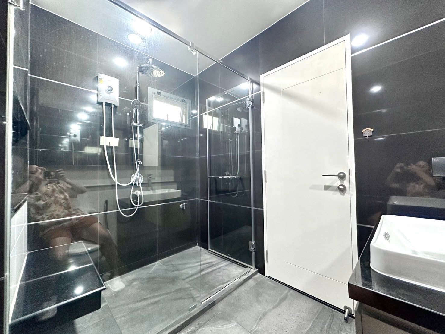 Detached House for rent in Bang Kapi, Bangkok - Modern bathroom with black tiles, glass shower enclosure, rain shower and vanity.
