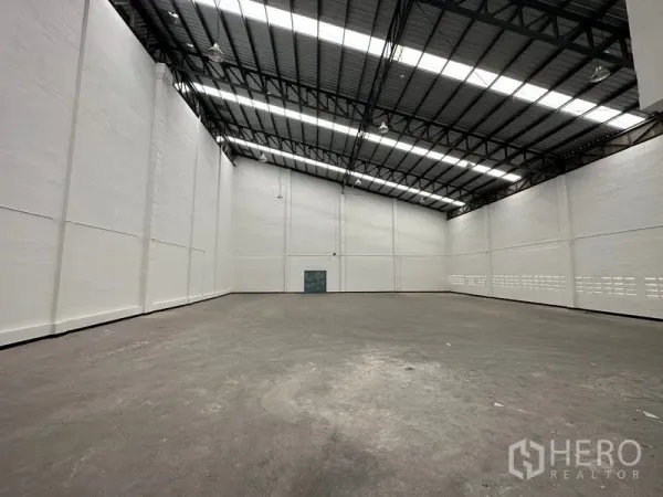 Factory for rent in Khlong Luang, Pathum Thani - Spacious empty warehouse interior with very high ceilings, steel roof trusses and skylight panels.