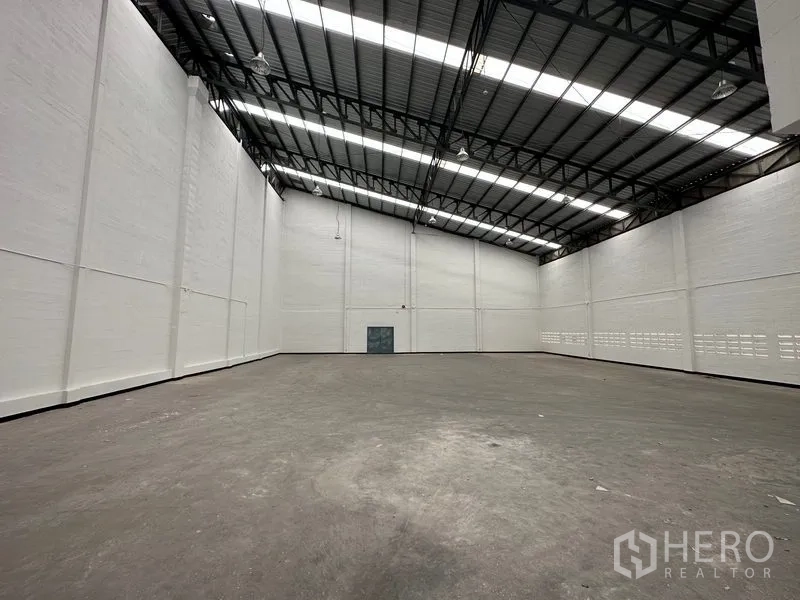 Factory for rent in Khlong Luang, Pathum Thani - Spacious empty warehouse interior with very high ceilings, steel roof trusses and skylight panels.