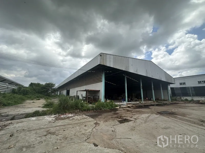 โรงงาน ขายในBang Bua Thong, Nonthaburi - ภายนอกโรงงานกรุเมทัลชีท มีช่องเปิดและลานขนถ่ายสินค้ากว้าง ใต้ท้องฟ้ามีเมฆ