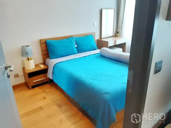 Condominium for rent in Khlong Toei, Bangkok - Cozy bedroom with double bed, wood flooring, bedside table and vanity by a large window.