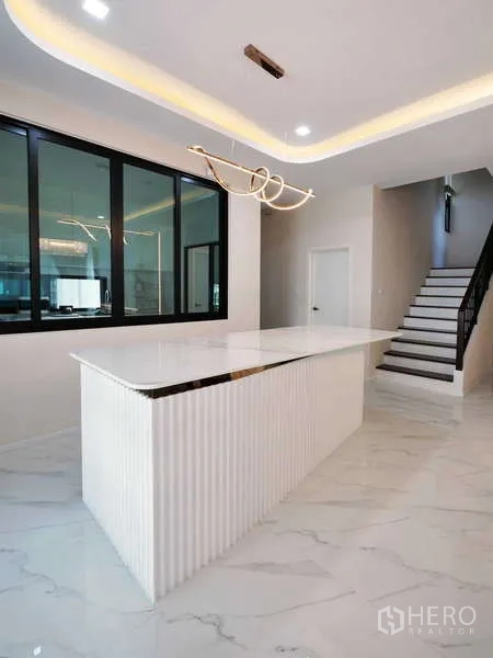 Detached House for rent or sale in Thanyaburi, Pathum Thani - Sleek island bar beneath sculptural pendant light beside the staircase with black handrail.