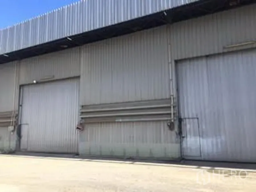 Warehouse for rent in Sai Mai, Bangkok - Close view of corrugated metal warehouse facade with dual loading bays and visible utility lines.