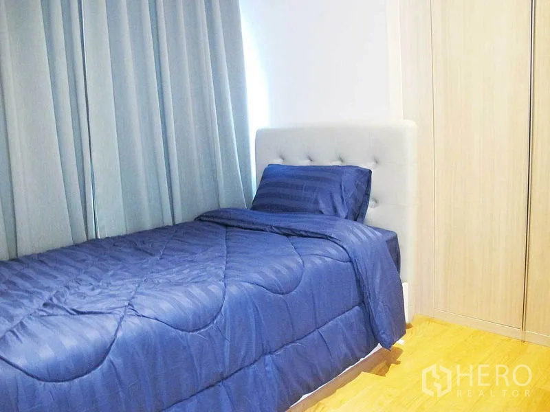 Condominium for rent in Watthana, Bangkok - Cozy second bedroom with single bed in blue linens, tall curtains and fitted wardrobe.