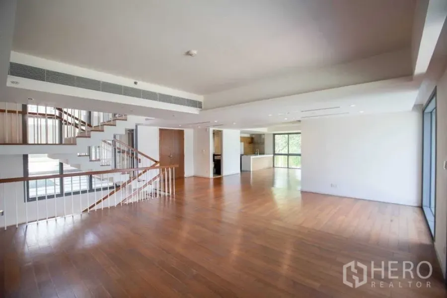 Condominium for rent in Yan Nawa, Bangkok - Large duplex living-dining area with staircase and floor-to-ceiling windows near open kitchen.