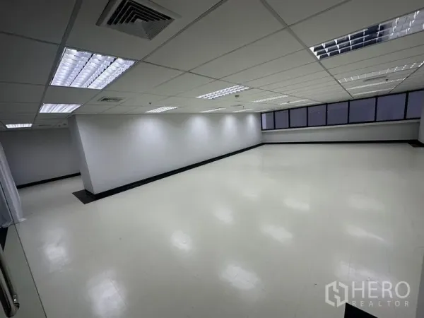 Office Space for rent - Open-plan 136 sq.m office interior in Ratchathewi, Bangkok with drop ceiling, fluorescent lights and a long window line.