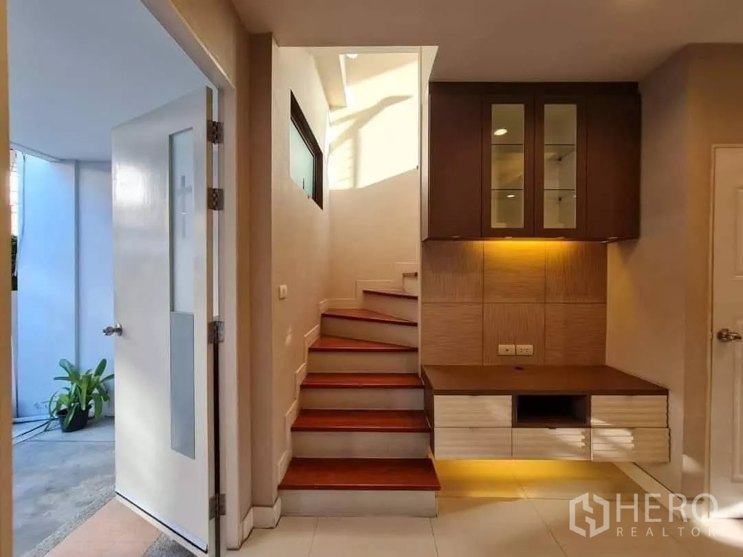 Townhouse for rent in Khlong Toei, Bangkok - Stair hall with wooden steps and illuminated built-in cabinet, opening to an outdoor area.