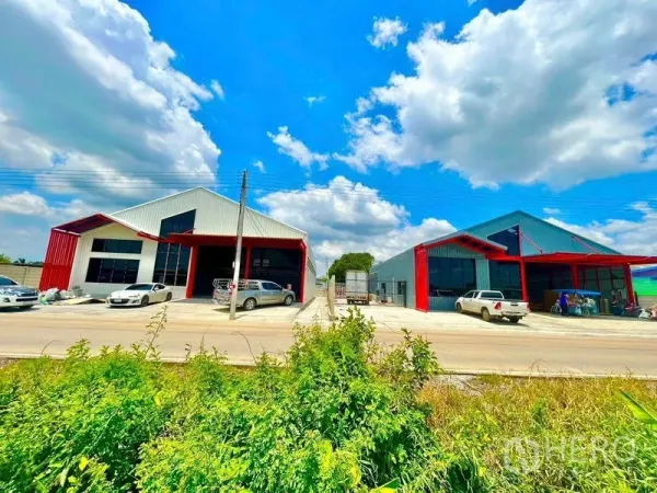Warehouse for rent in Lam Luk Ka, Pathum Thani - Street view of two modern red-framed warehouses with driveways and parking under a blue sky.