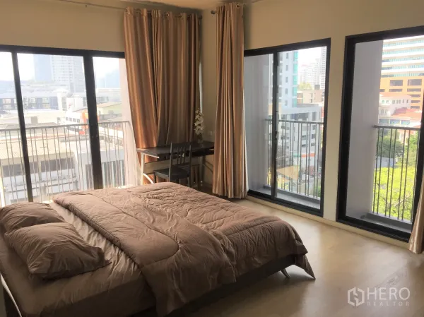 Condominium for rent in Watthana, Bangkok - Bright master bedroom with floor‑to‑ceiling windows, small balcony railings, curtains and a city view.
