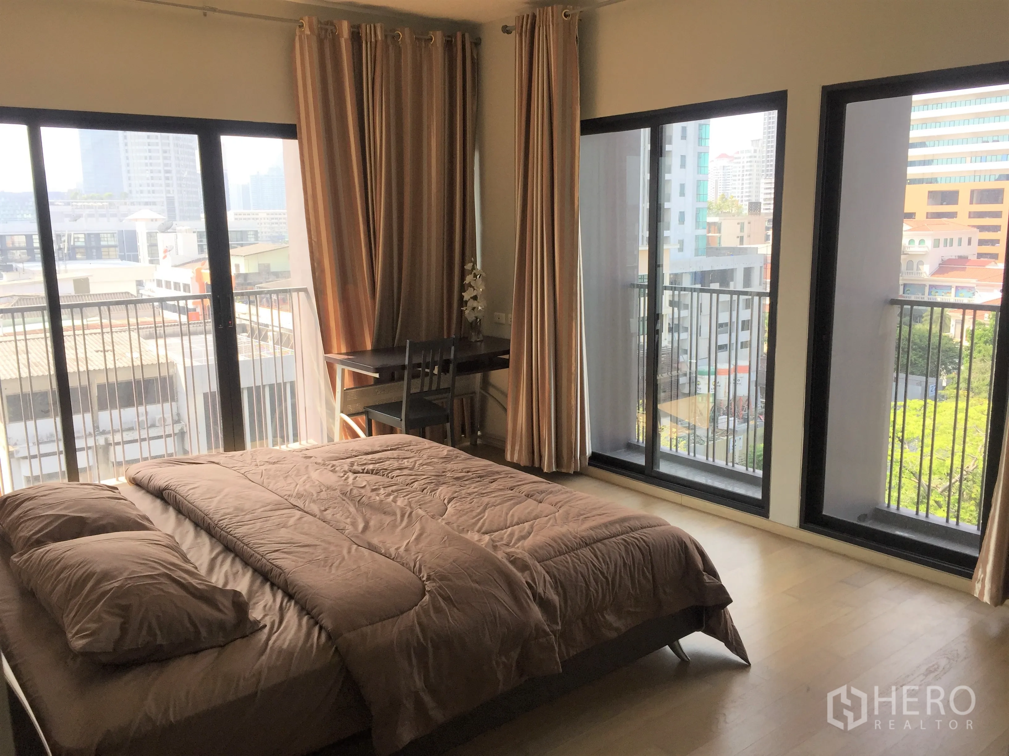 Condominium for rent in Watthana, Bangkok - Bright master bedroom with floor‑to‑ceiling windows, small balcony railings, curtains and a city view.
