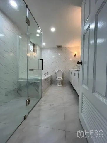 Condominium for rent in Khlong Toei, Bangkok - Spacious bathroom with glass-enclosed shower, bathtub, long vanity and marble-look walls and floors.