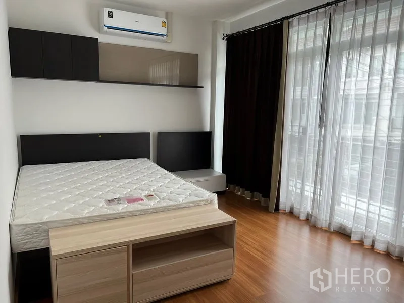 Townhouse for rent in Saphan Sung, Bangkok - Corner bedroom with balcony-height windows, sheer curtains and a queen bed.