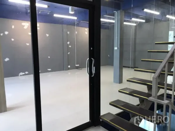 办公空间 出租在Watthana, Bangkok - 玻璃入户门与悬浮楼梯通向明亮的灰墙办公区。