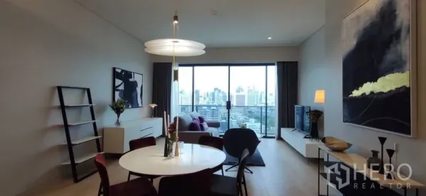 Condominium for rent or sale in Watthana, Bangkok - Open-plan living and dining area with round table, sofa, and a balcony overlooking the Bangkok skyline.