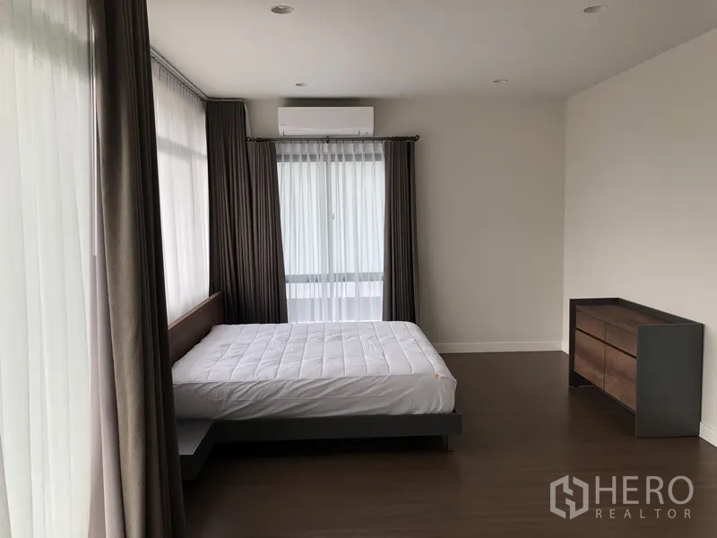 Detached House for rent in Bang Kapi, Bangkok - Spacious master bedroom with large windows, air conditioner, and wood flooring.