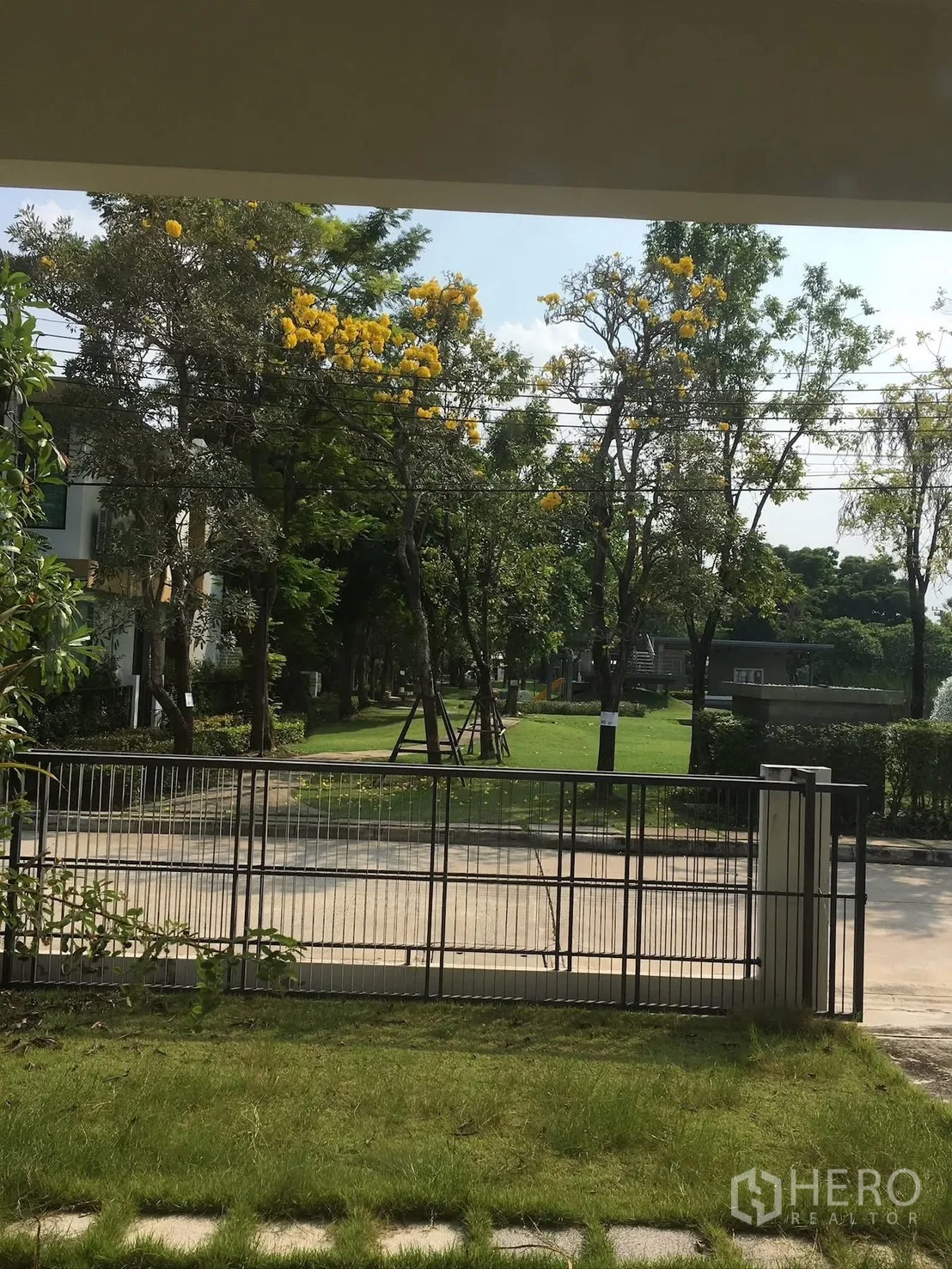 Detached House for rent in Bang Na, Bangkok - Front garden and fence overlooking a green park with flowering trees.
