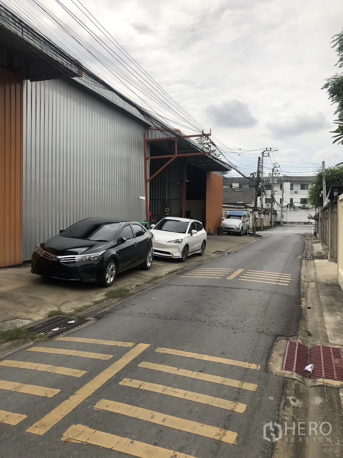 Warehouse for rent in Bueng Kum, Bangkok - Exterior view of the warehouse along a quiet lane with roadside parking and easy truck access.